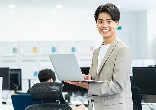 請求・振込代行サービスのイメージ - プロフェッショナルな男性がオフィスでラップトップを持って立っている様子