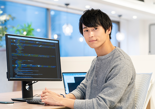 IT導入支援サービスのイメージ - プロフェッショナルな男性がオフィスでデュアルモニターを使ってコーディング作業をしている様子